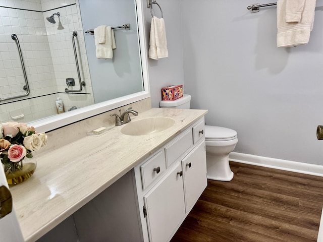 full bath featuring toilet, tiled shower, wood finished floors, and vanity