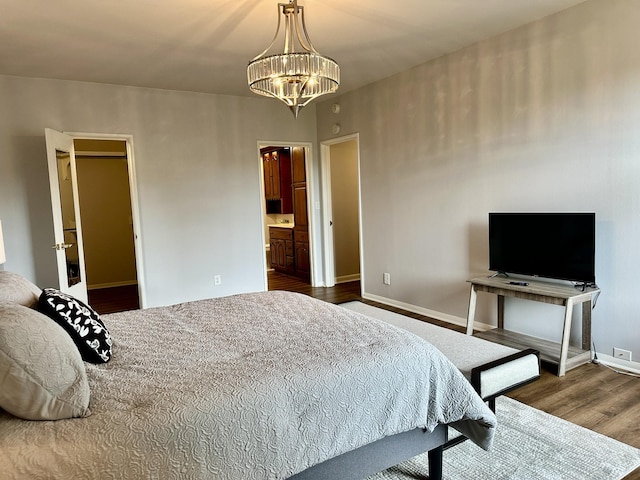 bedroom featuring connected bathroom, baseboards, a notable chandelier, and wood finished floors