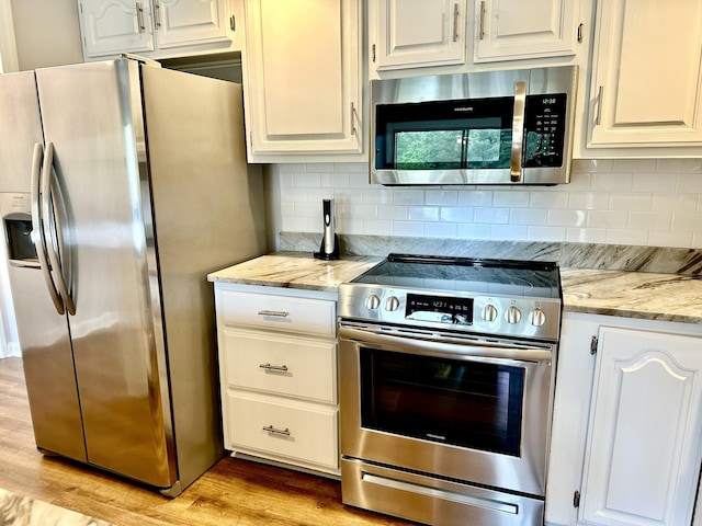 kitchen with white cabinets, appliances with stainless steel finishes, light stone counters, light wood-style floors, and tasteful backsplash