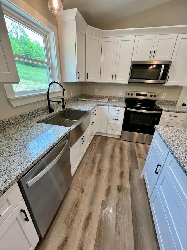 kitchen featuring light stone countertops, white cabinets, a sink, light wood-style flooring, and appliances with stainless steel finishes