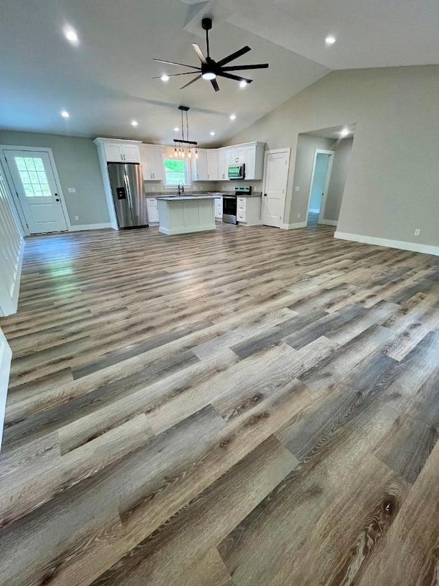 unfurnished living room featuring baseboards, ceiling fan, wood finished floors, and vaulted ceiling