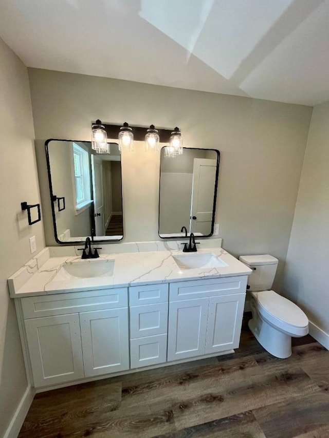 full bath with double vanity, toilet, a sink, and wood finished floors