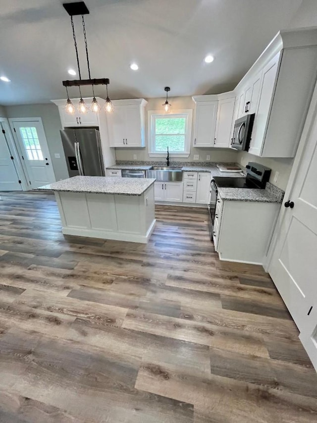 kitchen with a kitchen island, hanging light fixtures, a sink, white cabinets, and stainless steel appliances