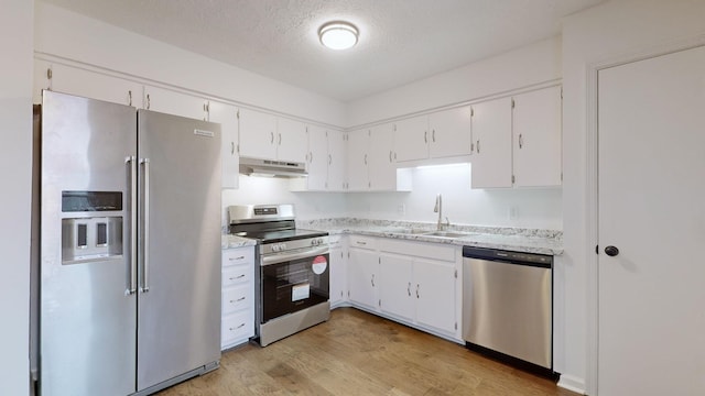 kitchen with white cabinetry, under cabinet range hood, a sink, light wood finished floors, and stainless steel appliances
