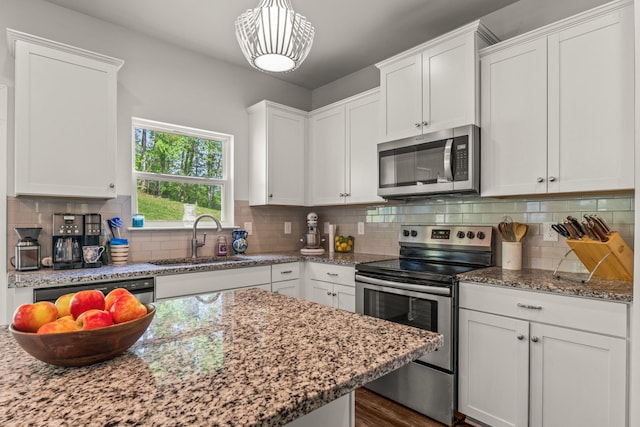 kitchen with a sink, appliances with stainless steel finishes, light stone countertops, and white cabinetry