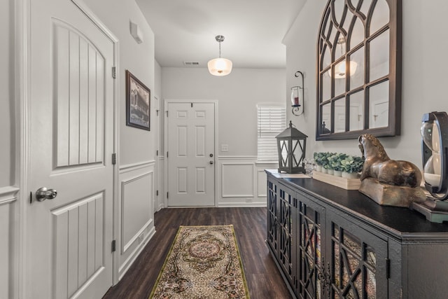 hall with dark wood finished floors, wainscoting, visible vents, and a decorative wall
