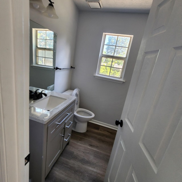 half bath featuring vanity, visible vents, wood finished floors, toilet, and baseboards