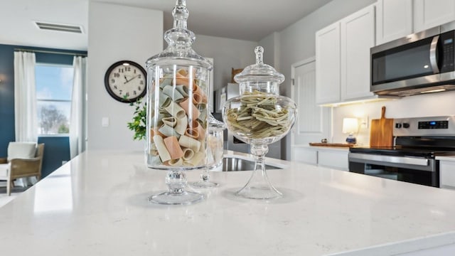 kitchen featuring appliances with stainless steel finishes, white cabinets, light stone countertops, and visible vents