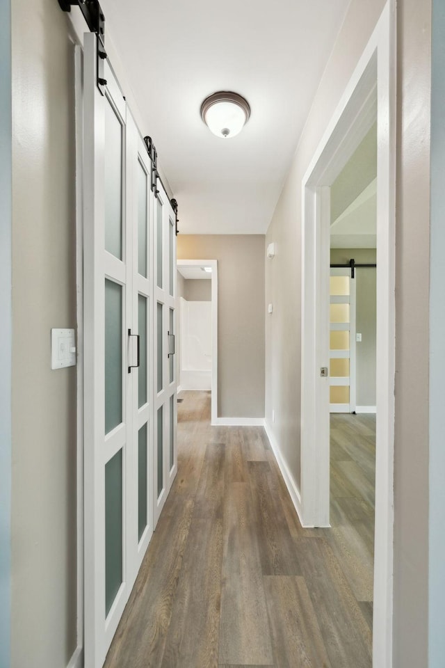 hallway with dark wood-style flooring, baseboards, and a barn door