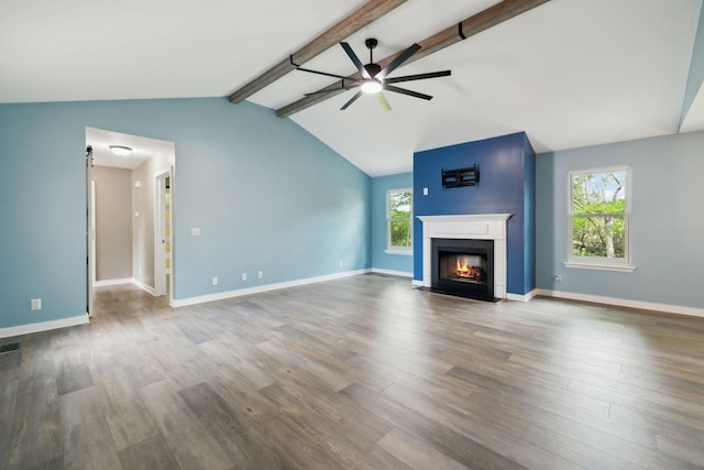 unfurnished living room featuring vaulted ceiling with beams, a ceiling fan, a fireplace with flush hearth, and wood finished floors