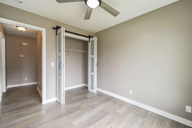 unfurnished bedroom featuring a barn door, light wood-style flooring, a ceiling fan, baseboards, and a closet