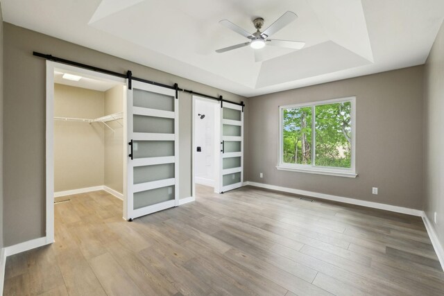 unfurnished bedroom with wood finished floors, a tray ceiling, a barn door, and a spacious closet