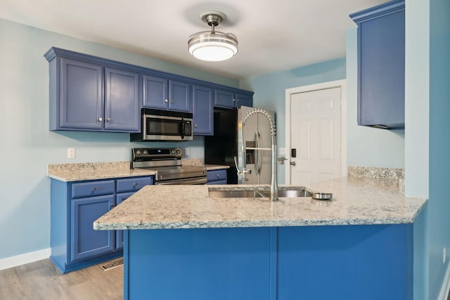 kitchen with blue cabinetry, a sink, a peninsula, stainless steel appliances, and light wood-style flooring