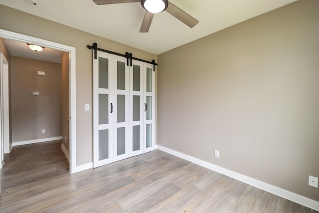 spare room featuring a ceiling fan, baseboards, a barn door, and wood finished floors