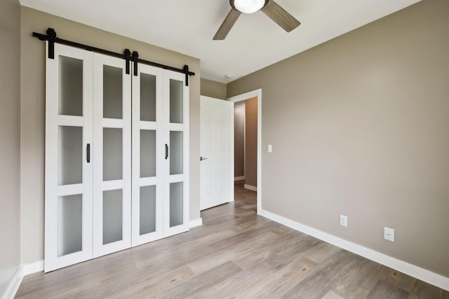 unfurnished bedroom featuring baseboards, a barn door, light wood finished floors, and ceiling fan