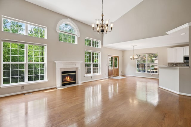 unfurnished living room with a premium fireplace, a chandelier, a wealth of natural light, and wood finished floors
