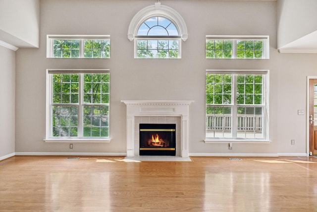 unfurnished living room featuring visible vents, a tiled fireplace, wood finished floors, baseboards, and a high ceiling