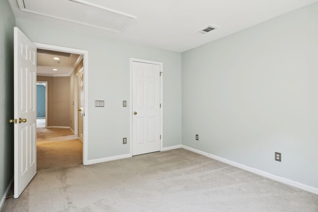 unfurnished bedroom featuring visible vents, attic access, baseboards, and light carpet