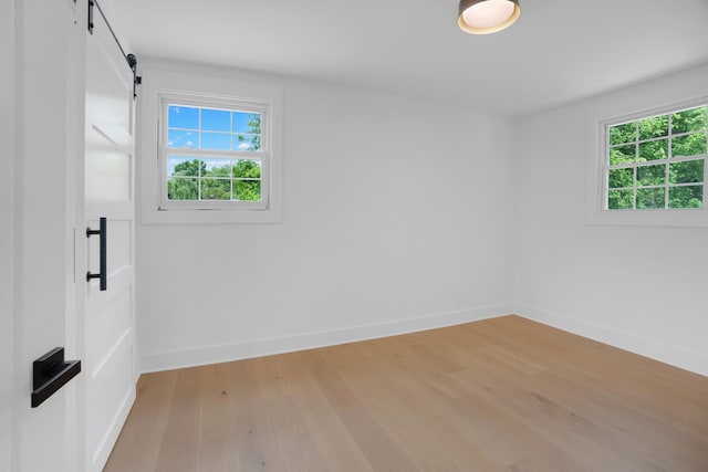 unfurnished room with plenty of natural light, a barn door, light wood finished floors, and baseboards