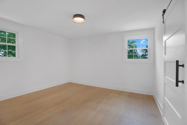 spare room featuring light wood-style floors, a barn door, and baseboards