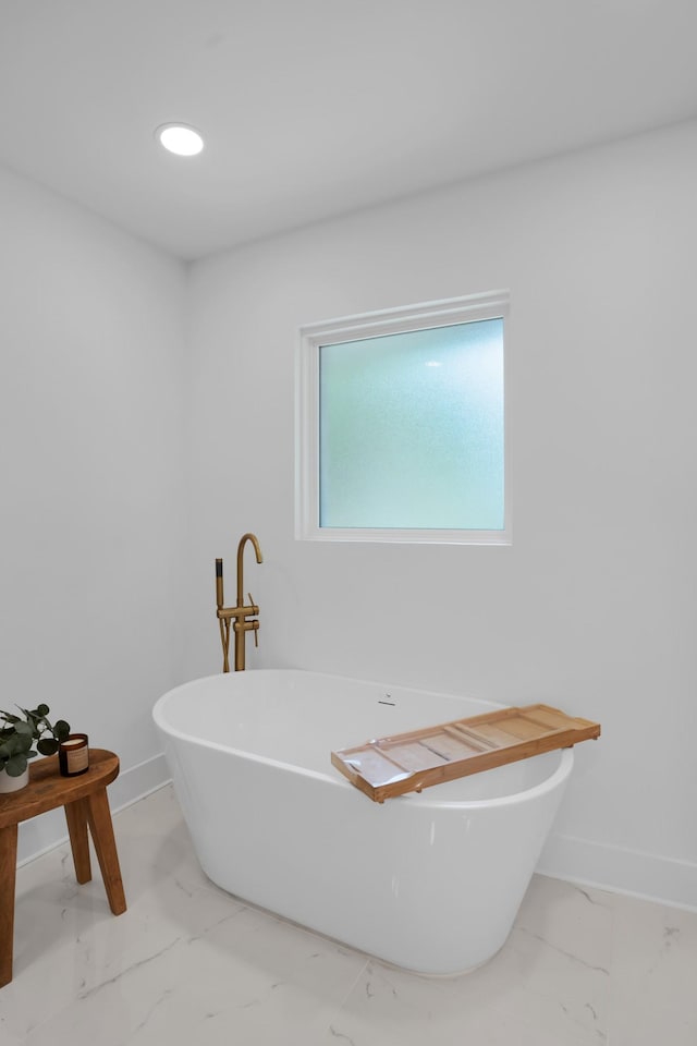 bathroom with a freestanding tub, baseboards, and marble finish floor