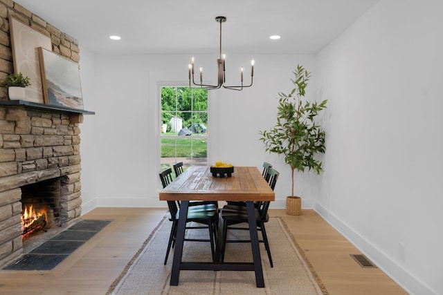 dining space with a stone fireplace, visible vents, baseboards, an inviting chandelier, and light wood-style flooring