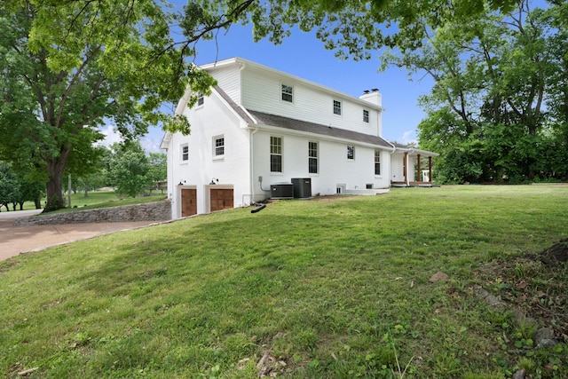 back of house featuring a chimney, a garage, central AC, a yard, and concrete driveway