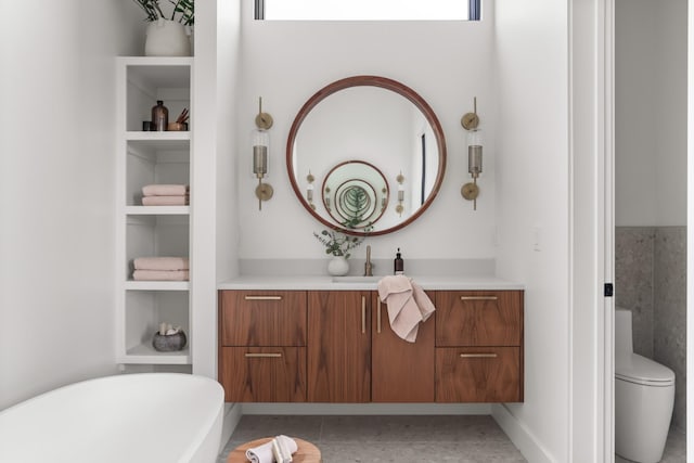 bathroom with a freestanding bath, built in shelves, vanity, tile patterned floors, and toilet