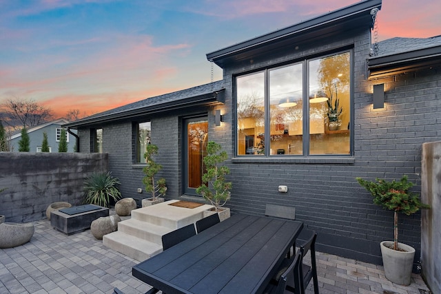 back of house at dusk with outdoor dining area, a patio area, and brick siding