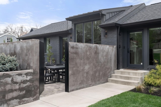 exterior space featuring brick siding, fence, and a shingled roof