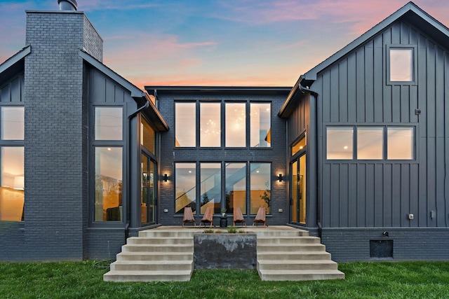 back of house at dusk featuring board and batten siding and a chimney