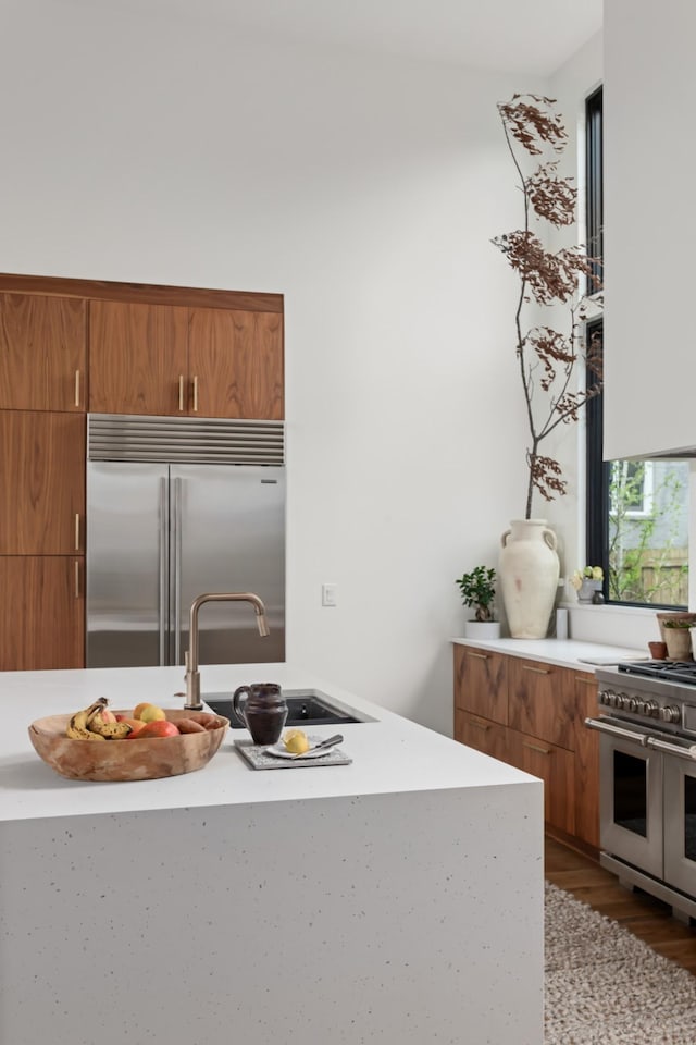 kitchen featuring brown cabinetry, wood finished floors, high end appliances, light countertops, and a sink