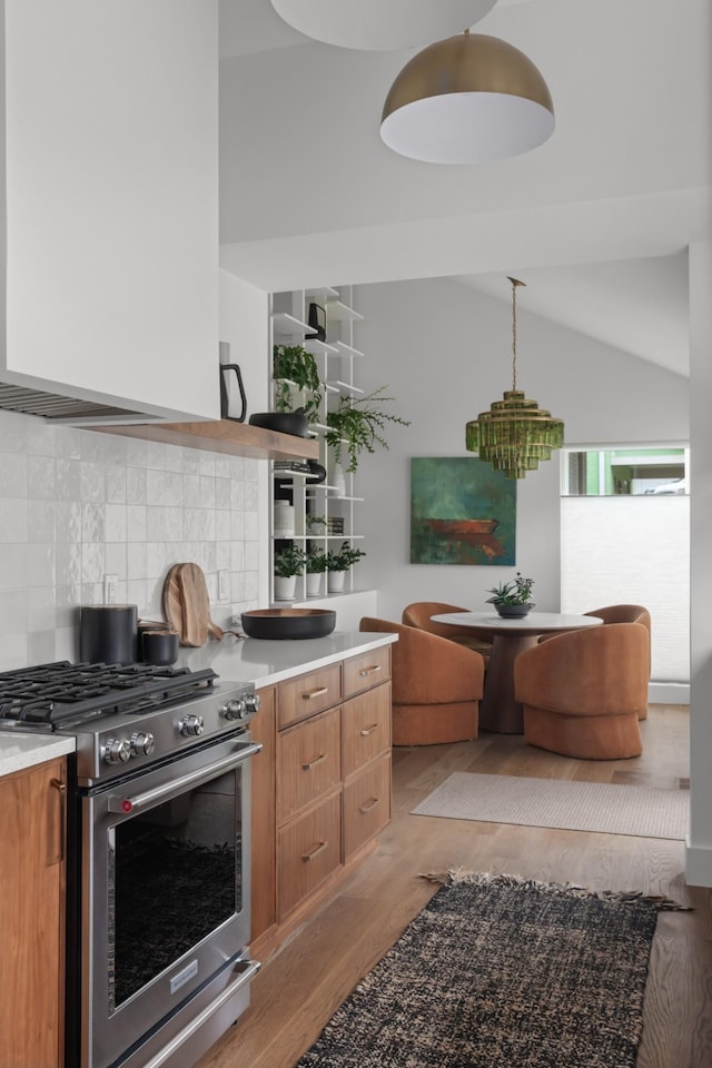 kitchen with brown cabinetry, backsplash, light wood-type flooring, light countertops, and high end stainless steel range