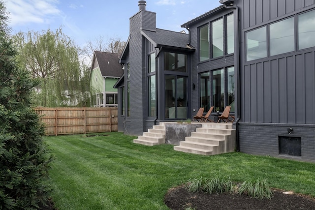 rear view of property featuring a lawn, fence, board and batten siding, and a chimney