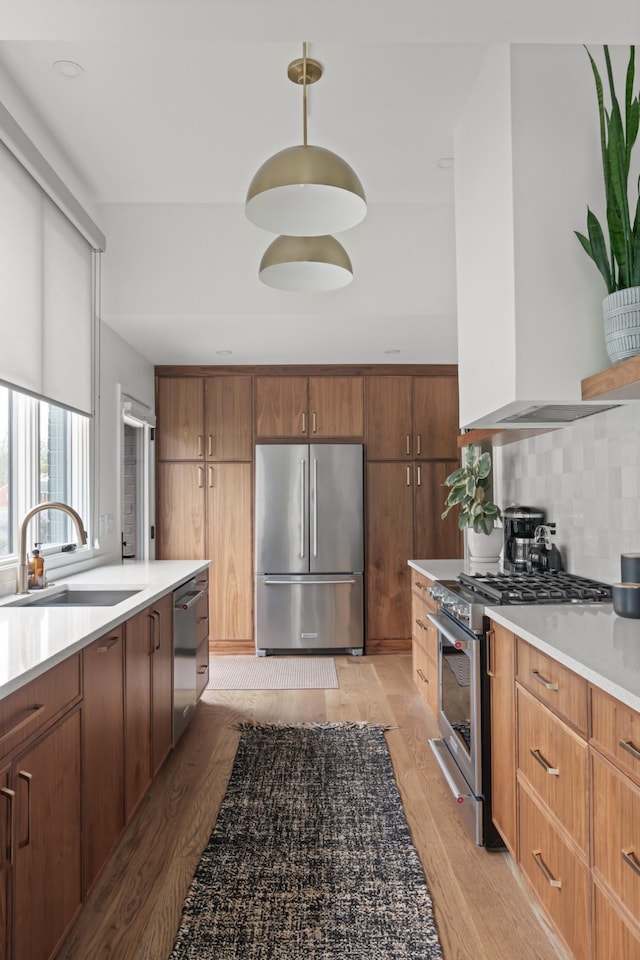 kitchen featuring wall chimney range hood, backsplash, light countertops, a sink, and stainless steel appliances