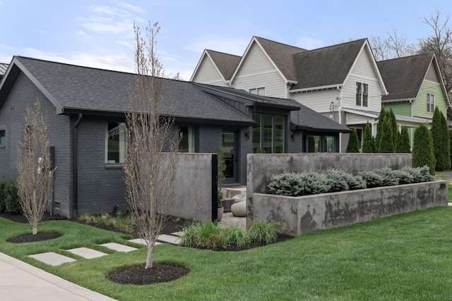 view of front of home with a shingled roof, a front lawn, and brick siding