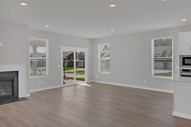 unfurnished living room featuring baseboards, recessed lighting, light wood-style flooring, and a glass covered fireplace