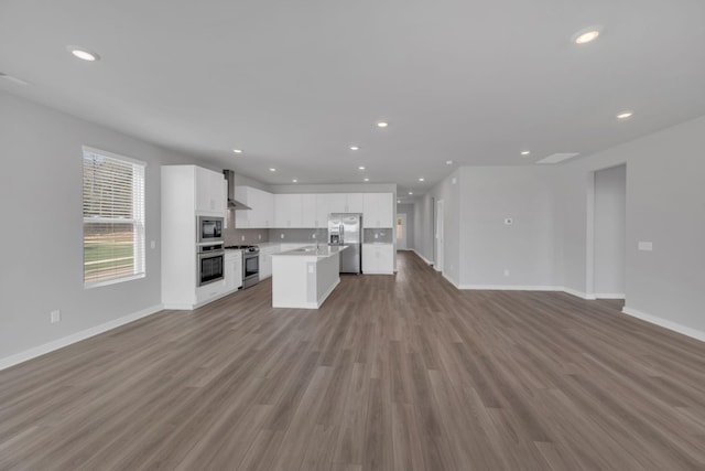 kitchen featuring wall chimney exhaust hood, stainless steel appliances, open floor plan, white cabinetry, and baseboards