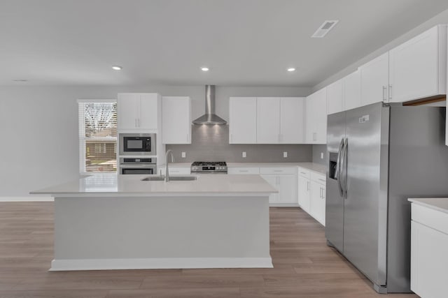 kitchen featuring visible vents, an island with sink, wall chimney exhaust hood, a sink, and stainless steel appliances