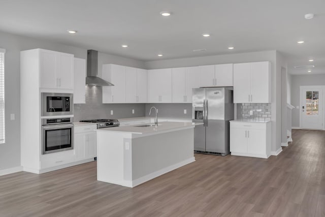 kitchen featuring appliances with stainless steel finishes, a sink, light countertops, wall chimney exhaust hood, and backsplash