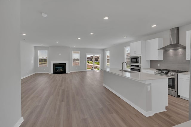 kitchen featuring wall chimney range hood, white cabinets, appliances with stainless steel finishes, and light wood-style flooring