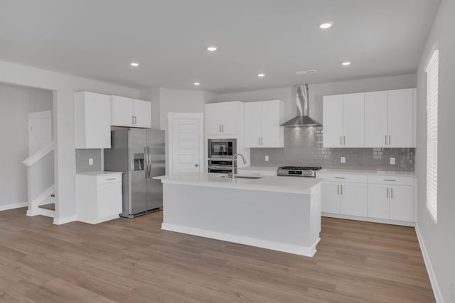 kitchen with appliances with stainless steel finishes, a sink, light countertops, wall chimney exhaust hood, and backsplash