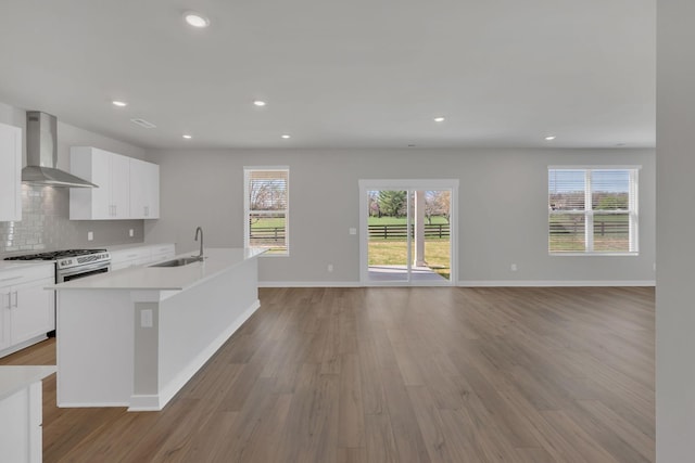 kitchen with wall chimney range hood, a kitchen island with sink, a sink, and light wood finished floors