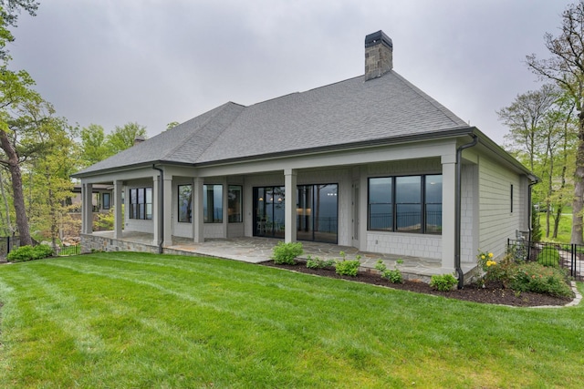 back of house with roof with shingles, a chimney, a yard, and a patio area