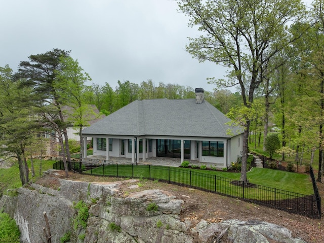 rear view of house featuring a fenced backyard, roof with shingles, a yard, and a chimney