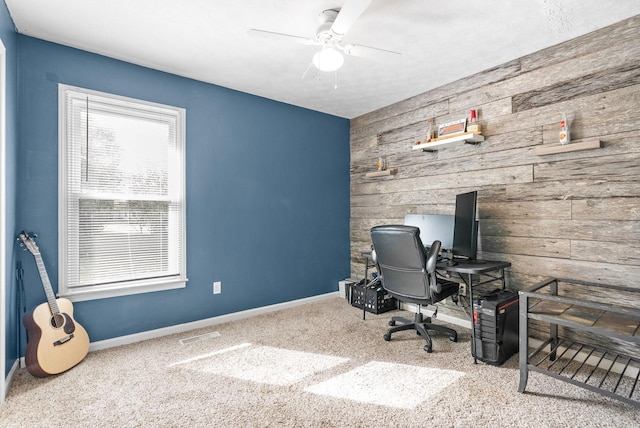 carpeted office space with wooden walls, baseboards, a ceiling fan, and visible vents