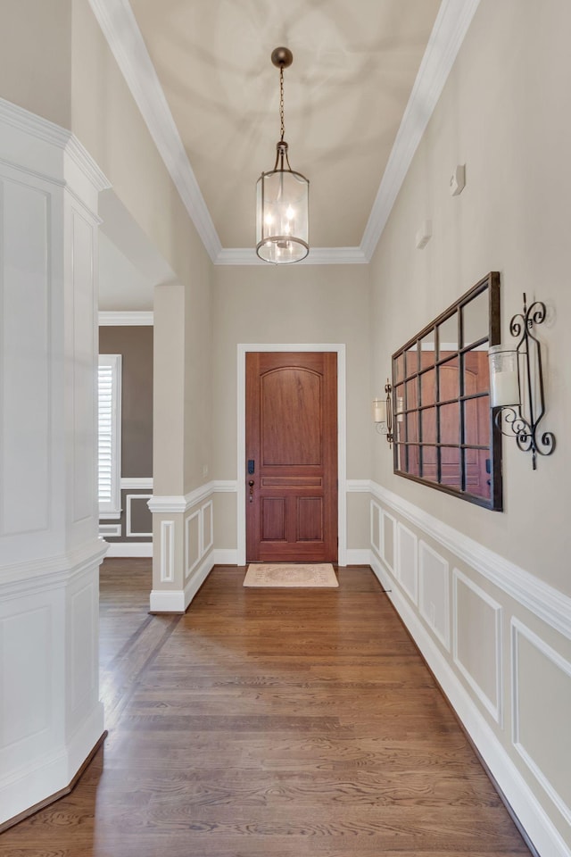 foyer entrance featuring a chandelier, ornamental molding, wood finished floors, and a decorative wall