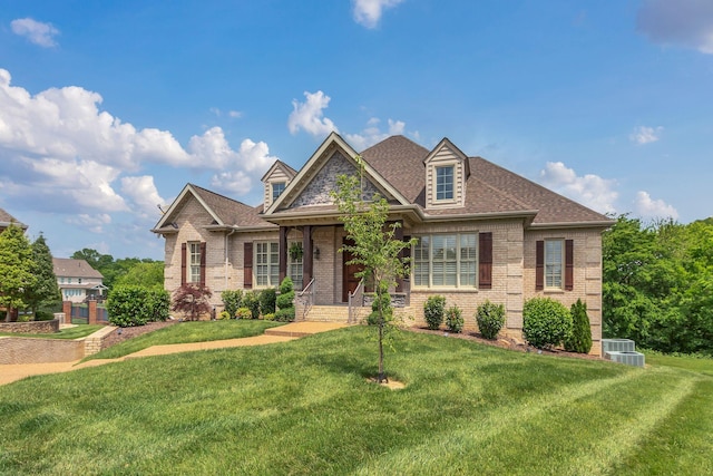 craftsman inspired home featuring brick siding, a shingled roof, a front yard, and central AC unit