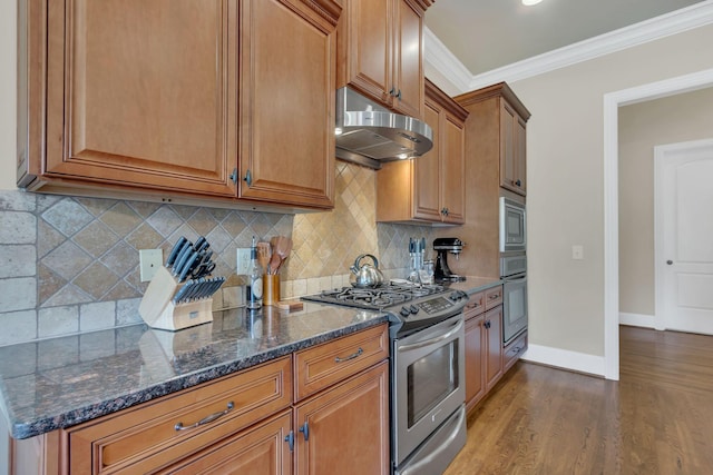 kitchen featuring appliances with stainless steel finishes, dark wood finished floors, brown cabinets, baseboards, and under cabinet range hood