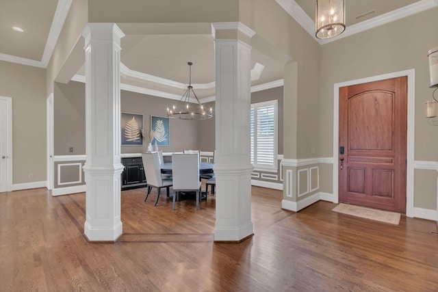 entryway featuring ornate columns, crown molding, wood finished floors, and a notable chandelier